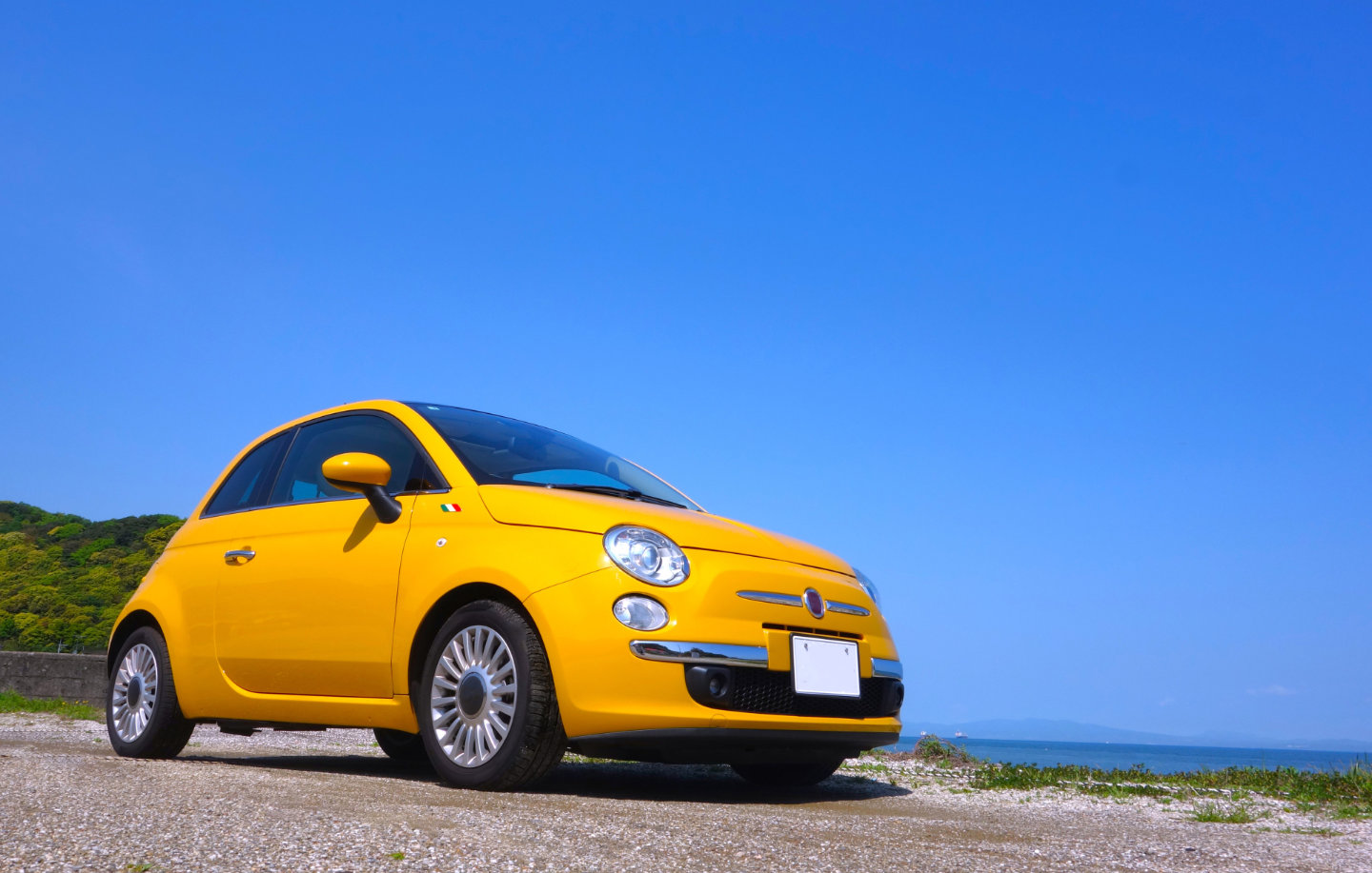 海辺を背景にしたイエローのフィアット500の中古車イメージ